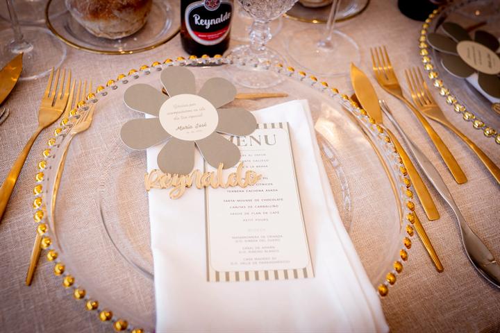 Mesa vestida con bajoplato dorado, menú y tarjeta en forma de flor